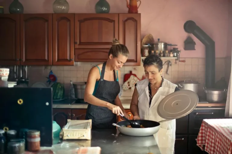 Two ladies stand in kitchen and making food in front of your cabinetry.