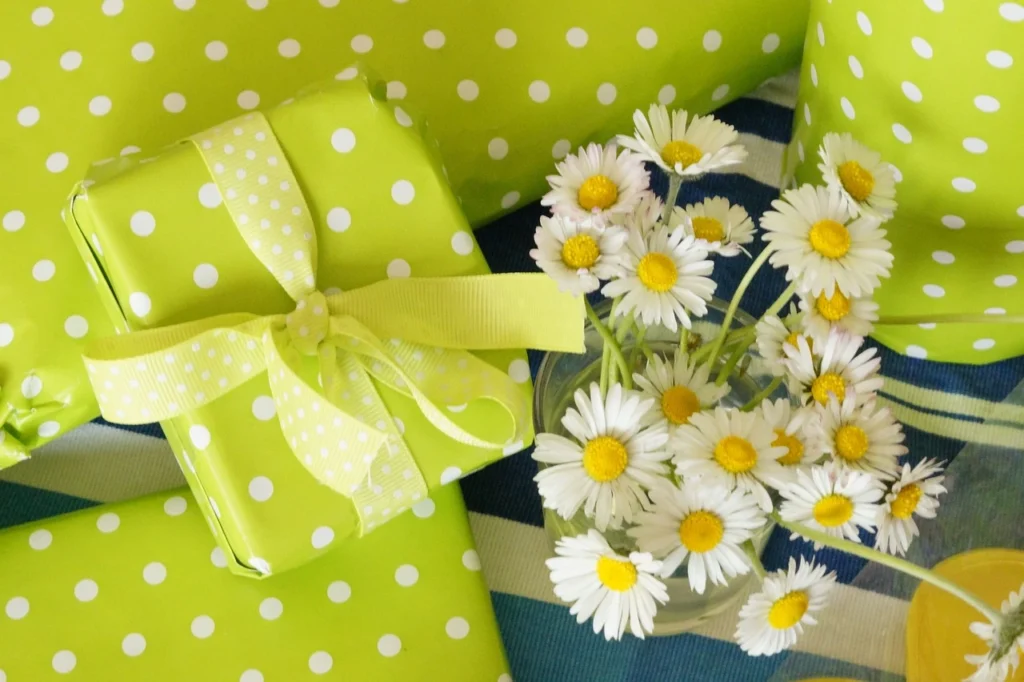 Green polka-dotted gift boxes with a yellow ribbon beside a small glass jar of white daisies.