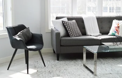 "Modern living room with grey sofa, black chair, glass coffee table, and light patterned carpet adding a cozy touch."