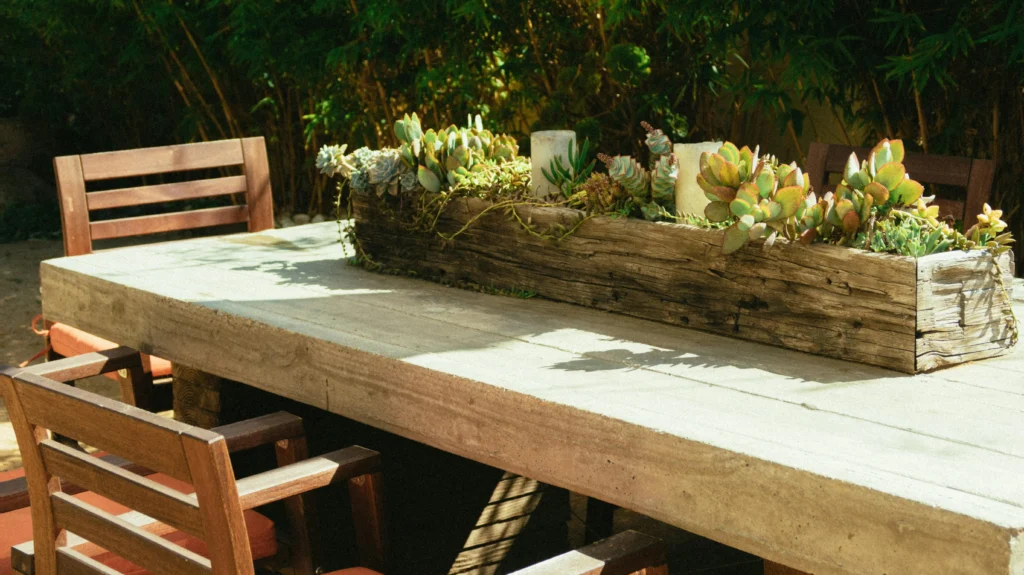 Outdoor garden dining table with wooden chairs and a rustic planter centerpiece featuring succulents, set in a peaceful backyard setting.